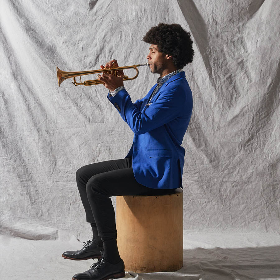Side photo of Wayne Tucker sitting on a stool playing the trumpet