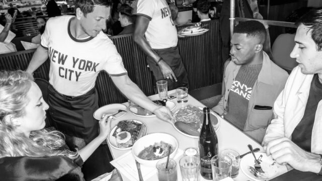 A group of people sitting at a booth being served dinner at Soho Diner at Soho Grand Hotel.