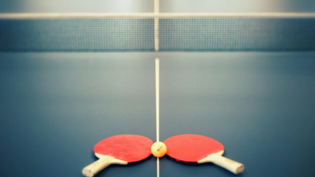 A ping pong table with 2 paddles and a ball.