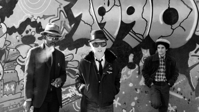 Black and white photograph of Fab 5 Freddy, Debbie Harry and Lee Quinones in front of a graffiti mural, taken in 1980 by photographer Bobby Grossman