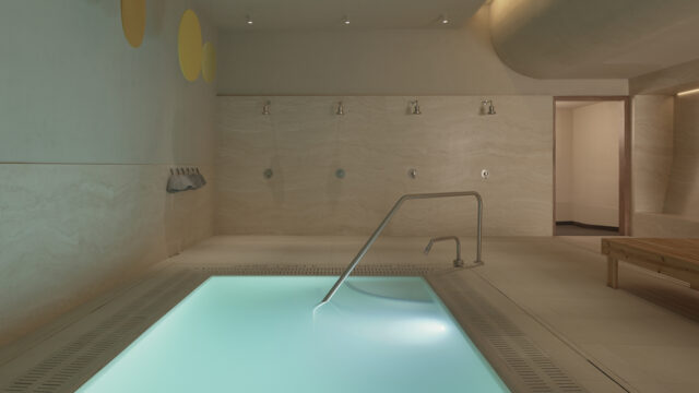 A serene plunge pool at Lore Bathing Club, New York, surrounded by warm travertine stone walls and flooring.