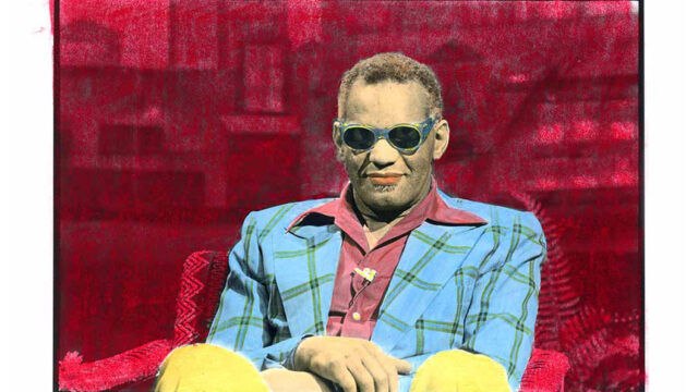 A hand-tinted portrait of Ray Charles seated in a chair wearing sunglasses, a blue plaid blazer, and yellow trousers against a vivid red backdrop. Photographed by Edie Baskin for Saturday Night Live.