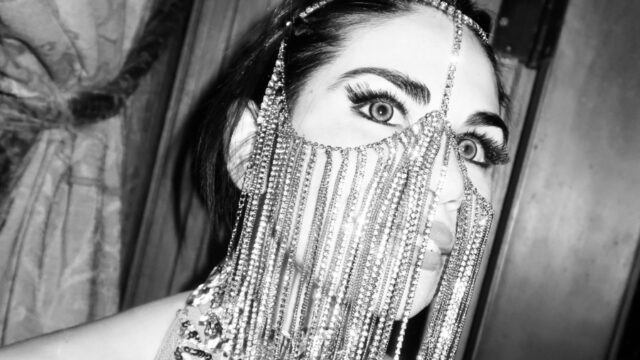 A woman at a party wearing a hanging bedazzled mask.