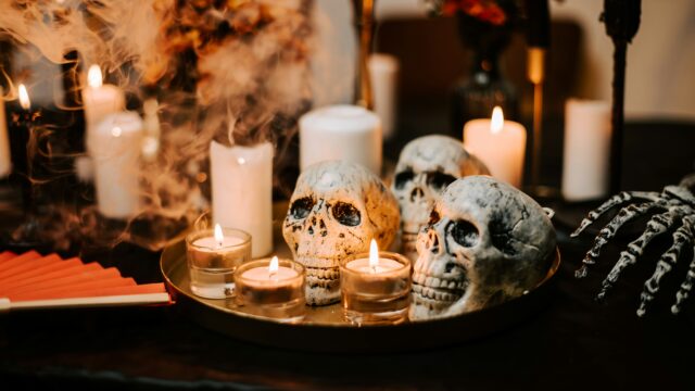 Faux skulls, flickering candles, and drifting smoke on a moody Halloween tabletop.