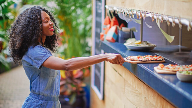 A Gilligan's waitress smiling whilst picking up a freshly baked pizza straight out of the firewood over station.