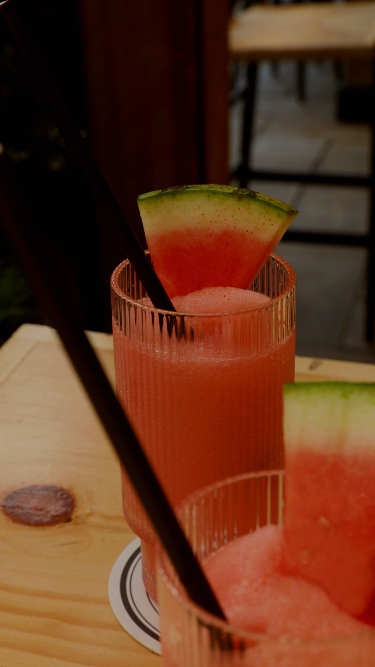 Red frozen drinks in see through glasses with a black straw and slice of watermelon.