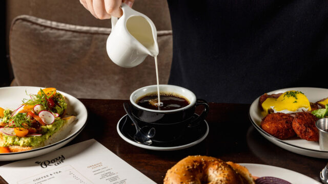 Man pouring creamer into a black coffee at Roxy Café in Tribeca.