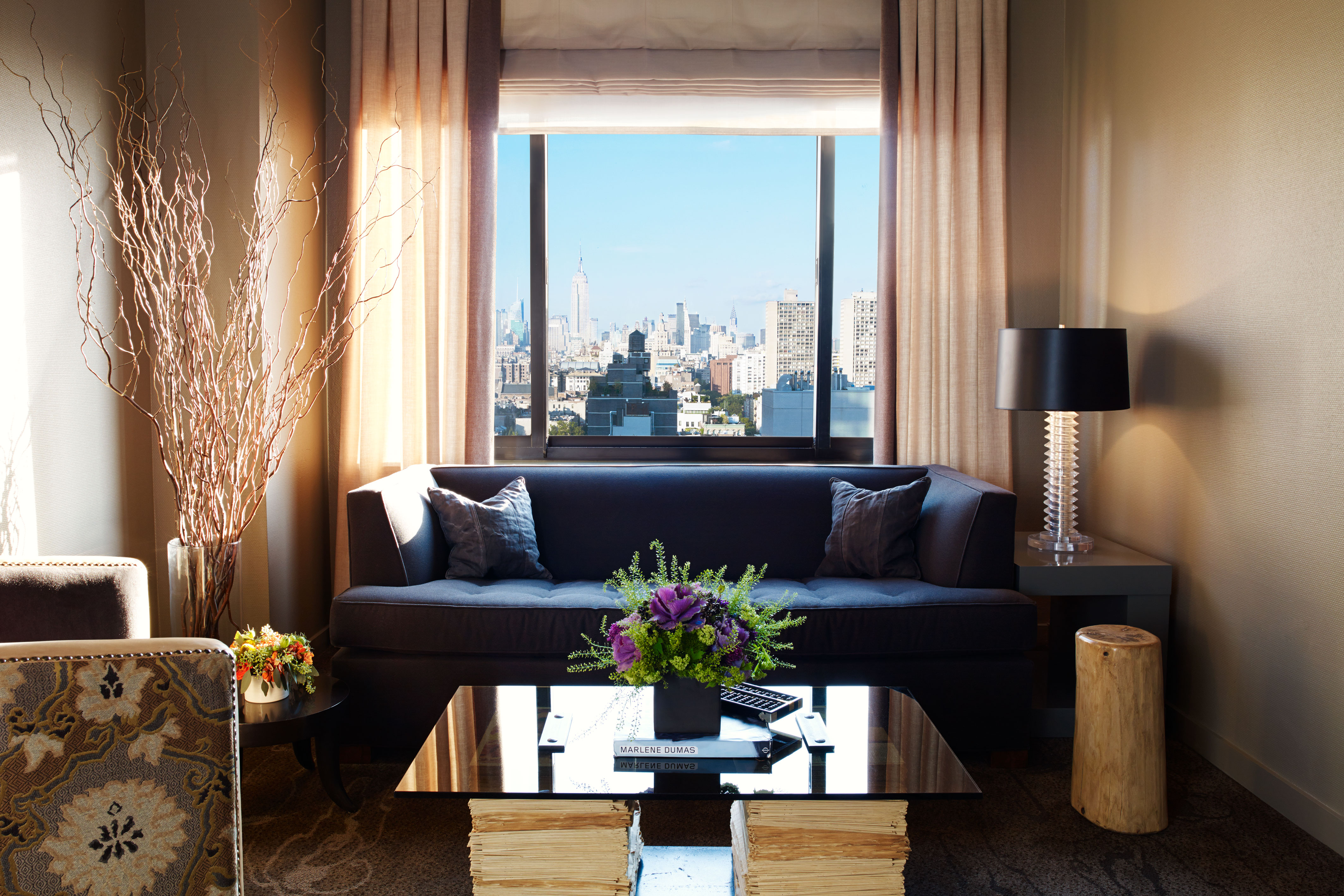 Deluxe One Bedroom Suite living rooo with a blue couch, coffee table with flowers and a plush chair. there is a view of the manhattan skyline