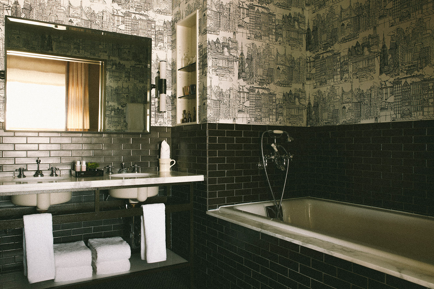 one bedroom suite bathroom with black subway tile and wallpaper details. There is a bathtub next to the sink