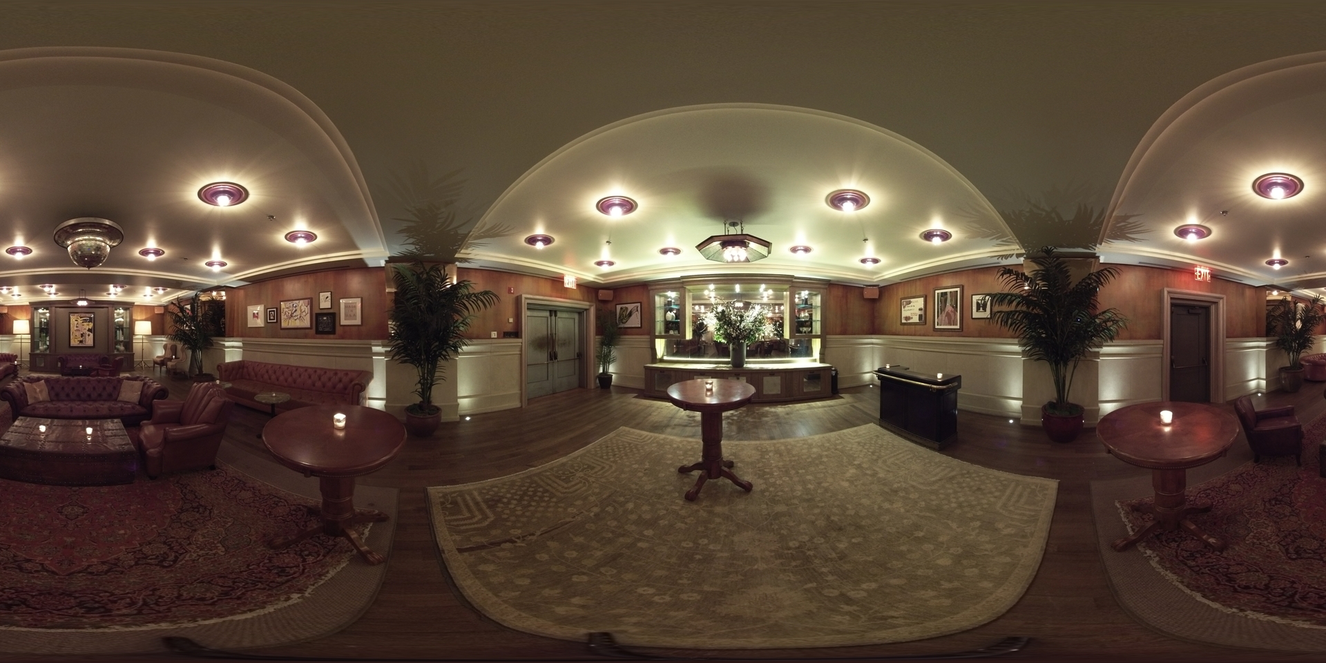 A wide-angle view of a hotel lobby with a high arched ceiling, chandeliers, couches, coffee tables, and plants.