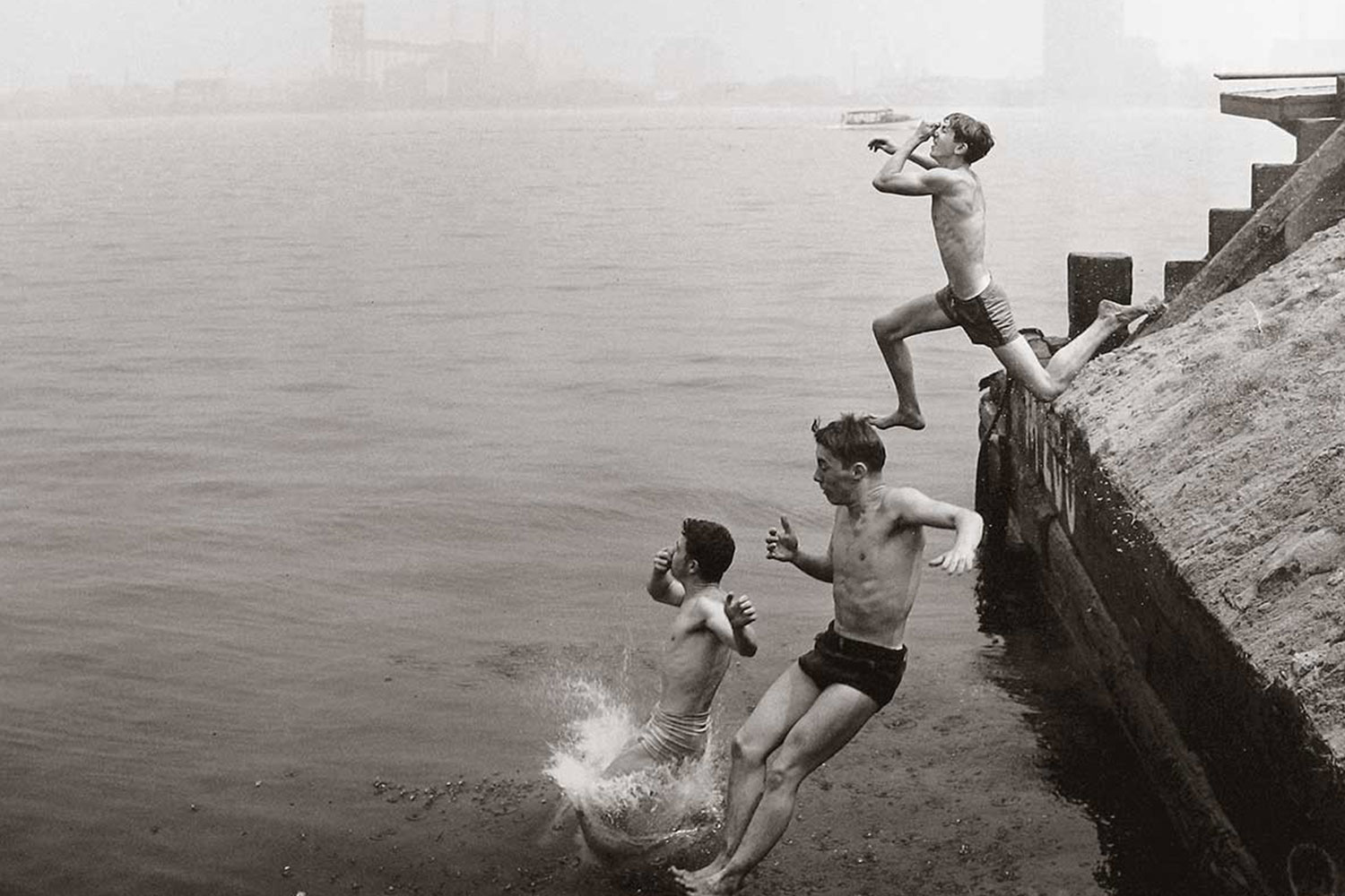 a black and white photo of three kids jumping into the water