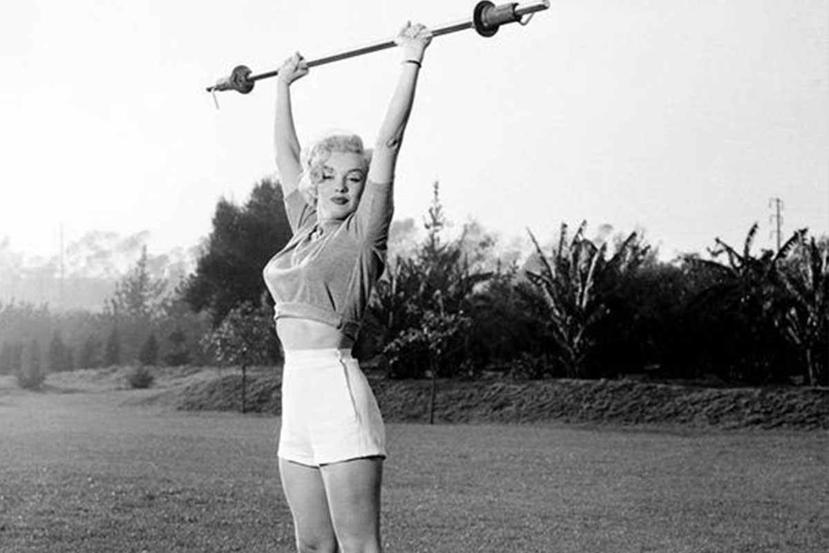 a black and white photo of Marilyn Monroe holding a dumb bell above her head