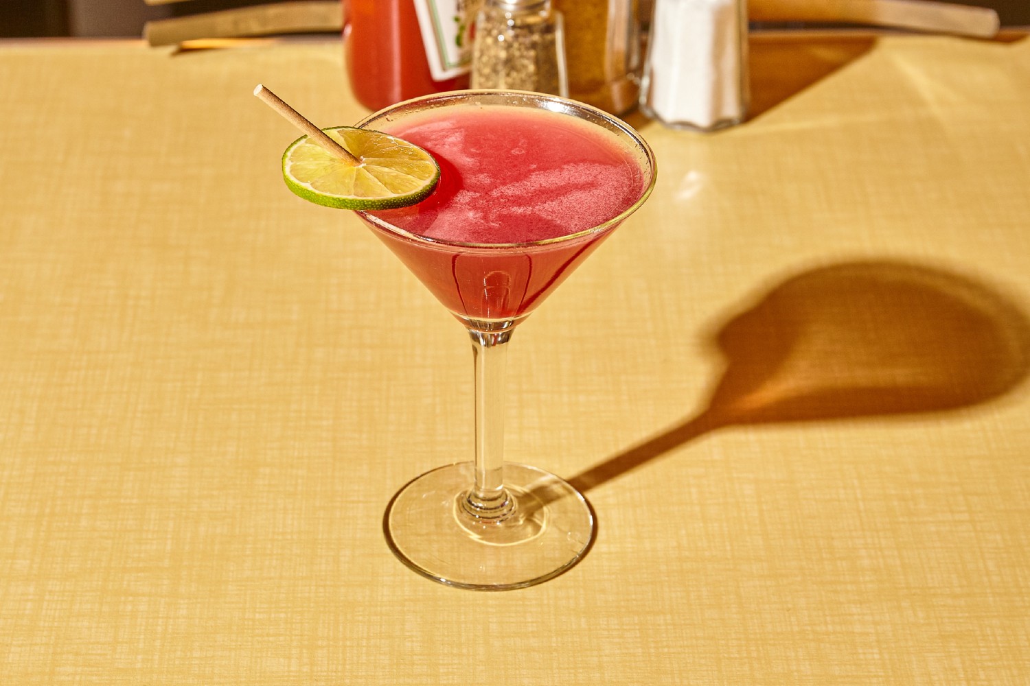 Martini glass filled with pink liquid and garnished with a lime and dowel.