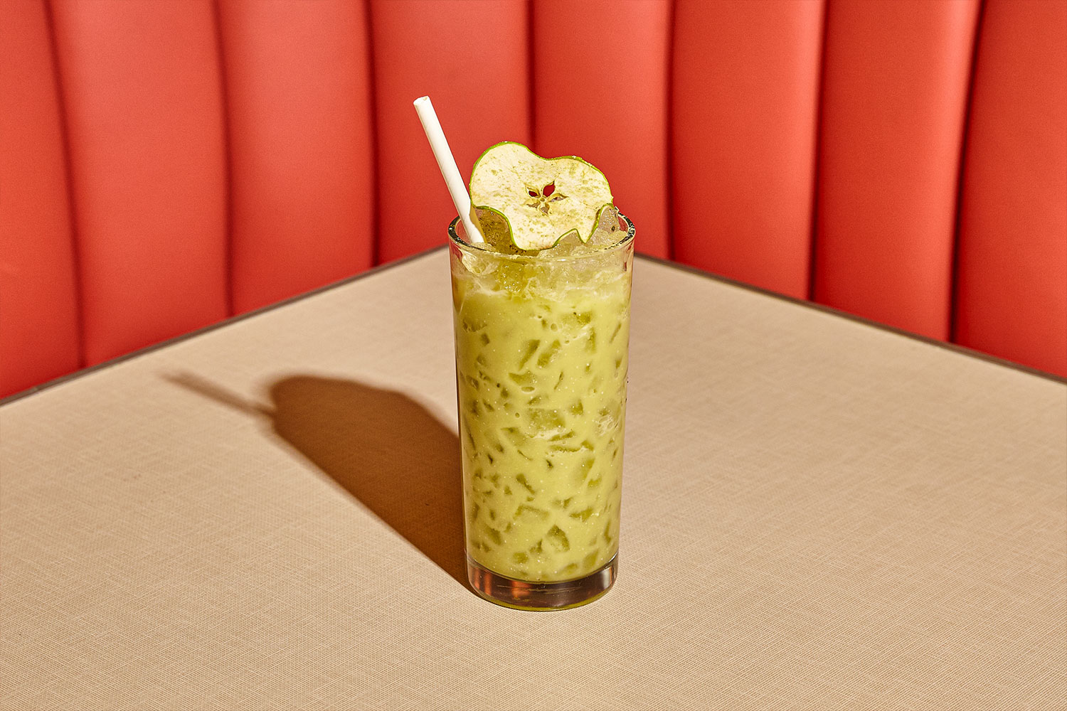 A green cocktail with a white flower garnish sits on a Soho Diner booth table