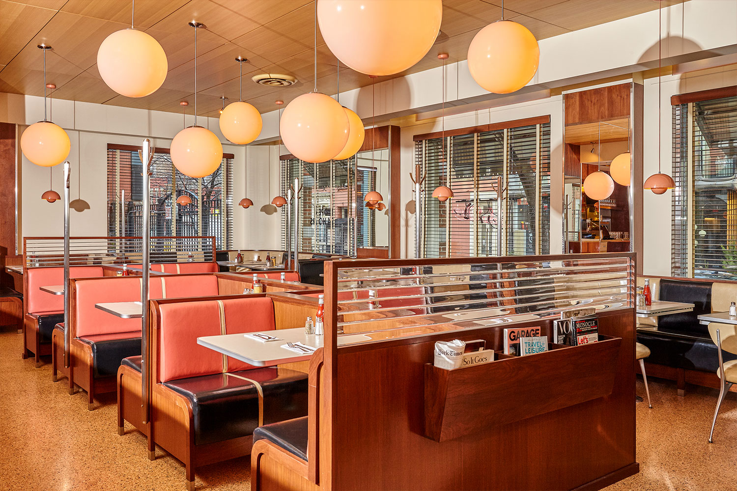 the interior of the soho diner. Red booths with dark wood line the space and there are large spherical lights hanging from the ceiling