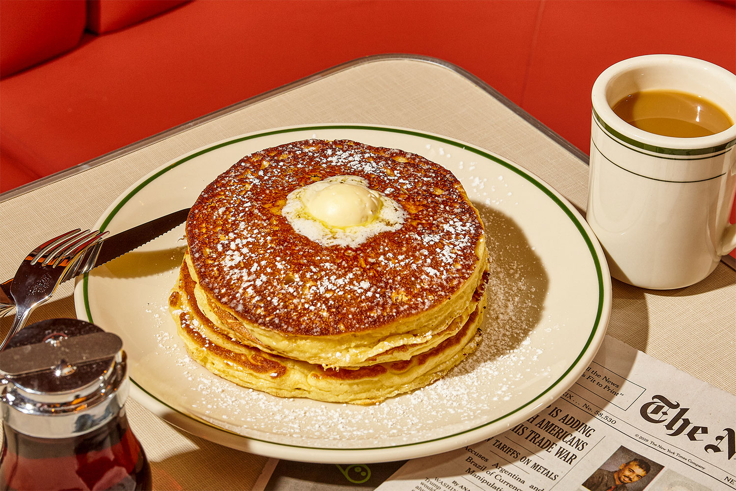 a shortstack of fluffy pancakes sprinkled with powdered sugar with a dollop of whipped butter