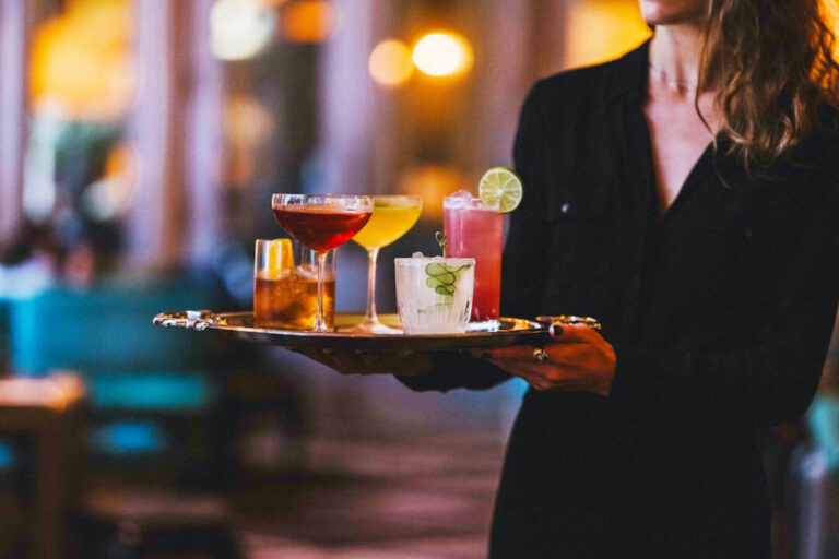 a woman carries a tray of craft cocktails