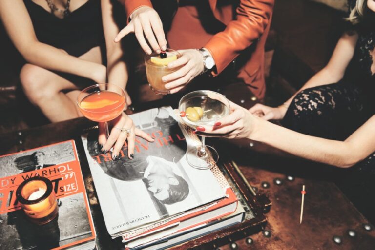 three party goers sit in a group and are raising their drinks in a cheers