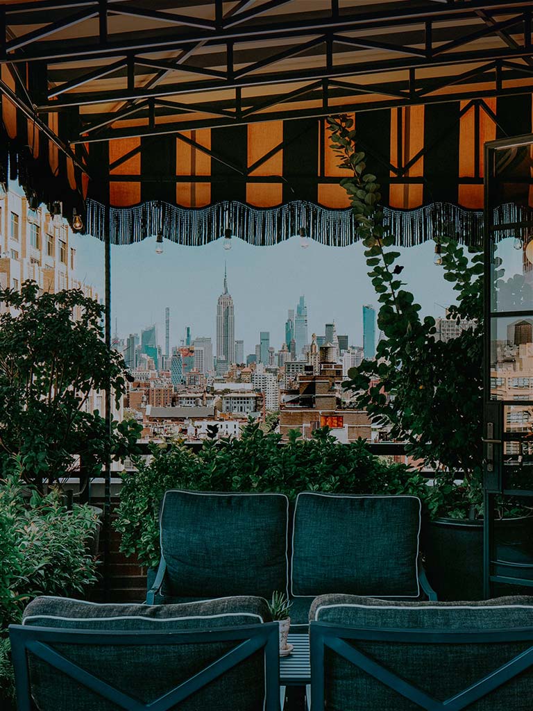 the outdoor terrace of the suite. there are blue velvet couches and a striped awning. there is a great view of midtonwn manhattan
