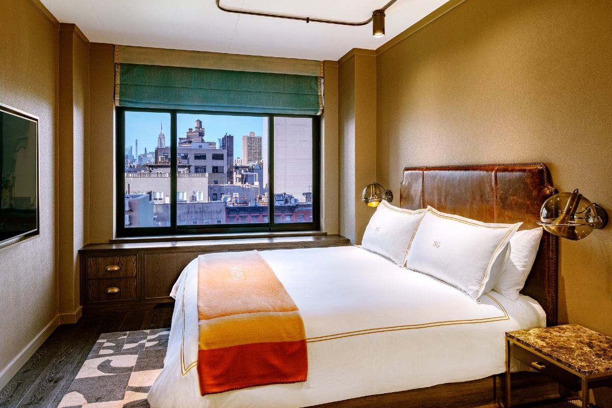 Guest Room at Soho Grand Hotel showing a king bed with white linens and an orange throw blanket and a New York City view from the window.