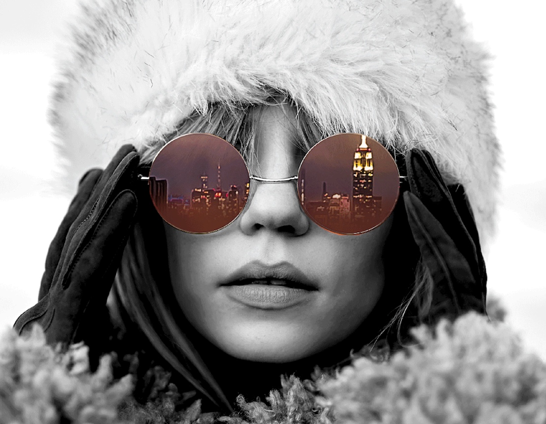 Woman with white fur hat wearing sunglasses that reflect the Empire State Building.