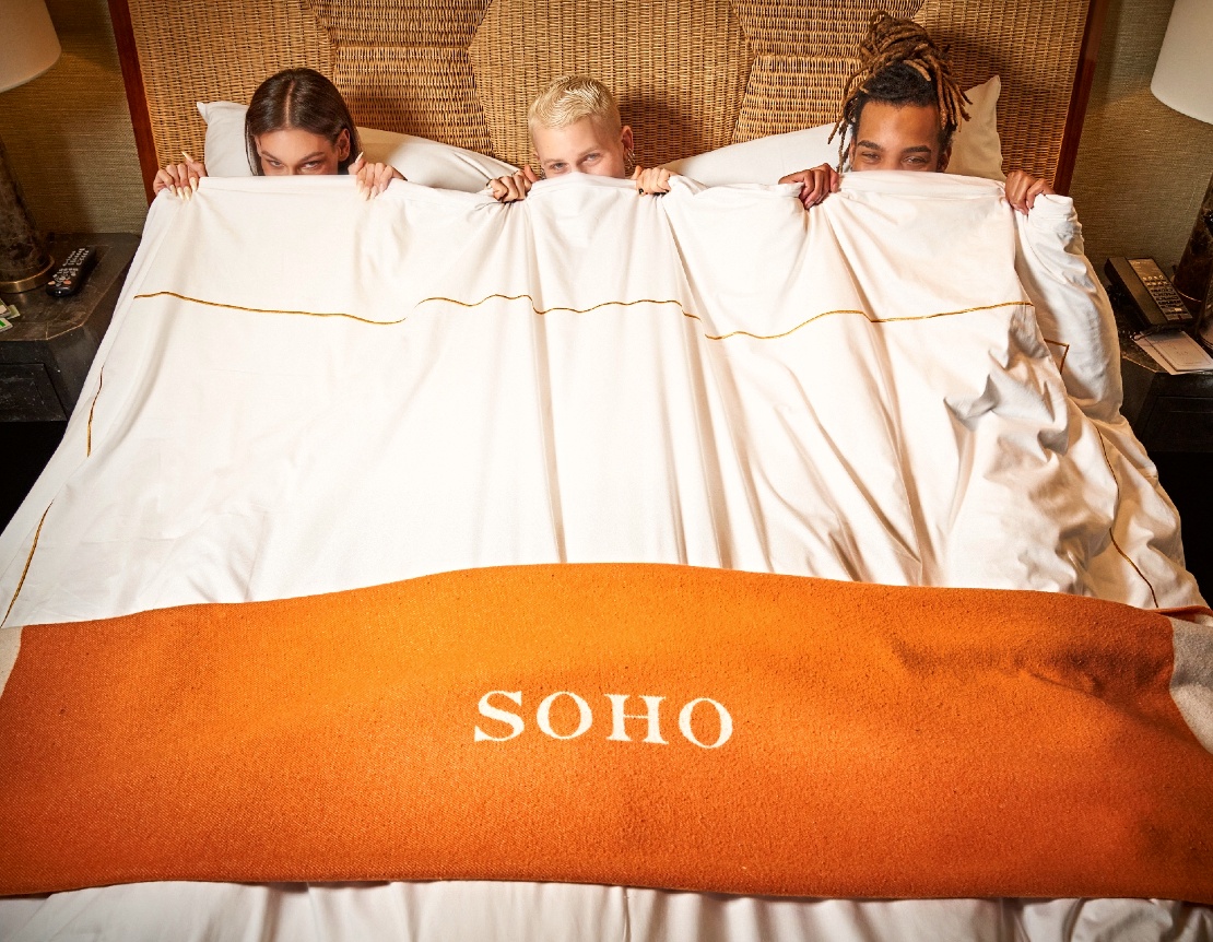 Three people in a king bed pulling the covers up above their lower faces.