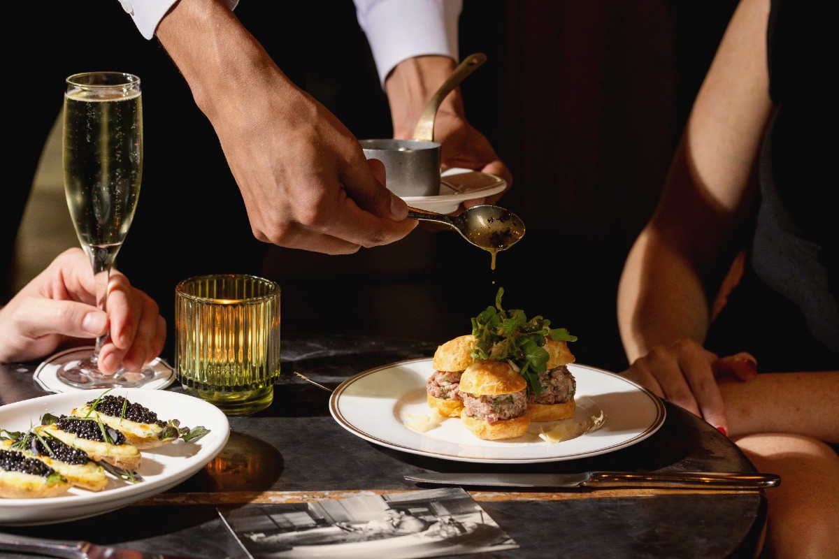 Hands of a waiter pouring sauce on a plated entree.