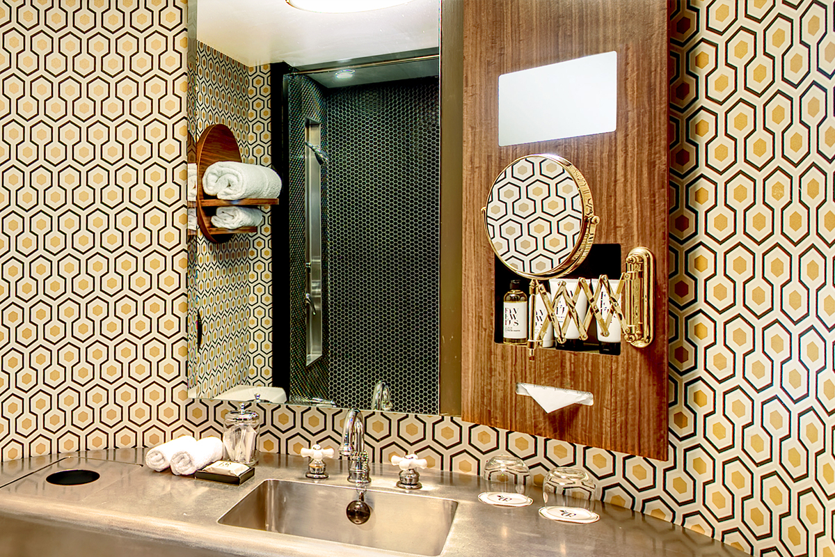 Roxy Hotel New Bathroom with geometric wallpaper, stainless steel sink, and black tile shower.