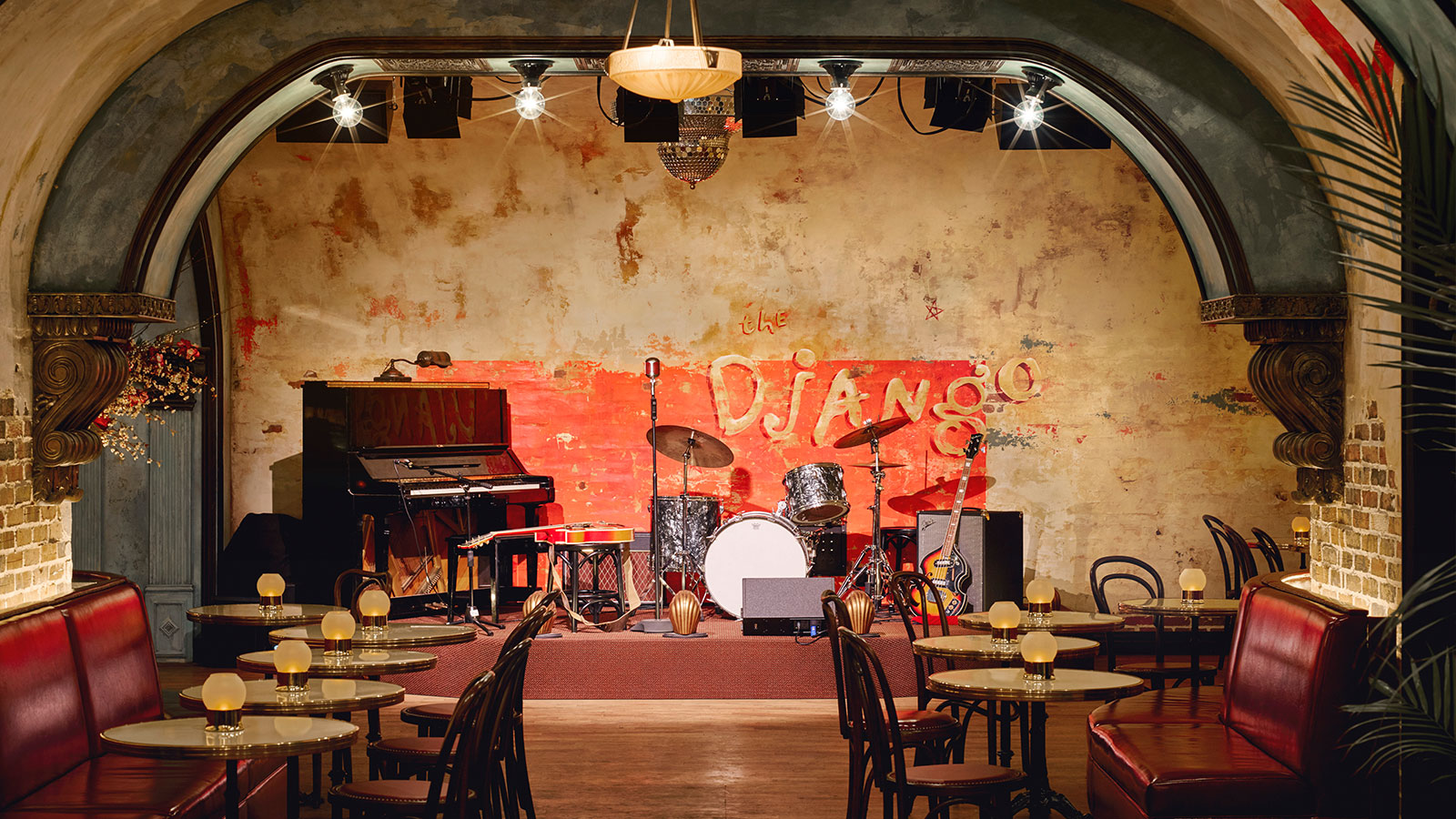 the django stage with all its instruments including a piano, a drum set and a guitar. There are candlelit tables lining the room