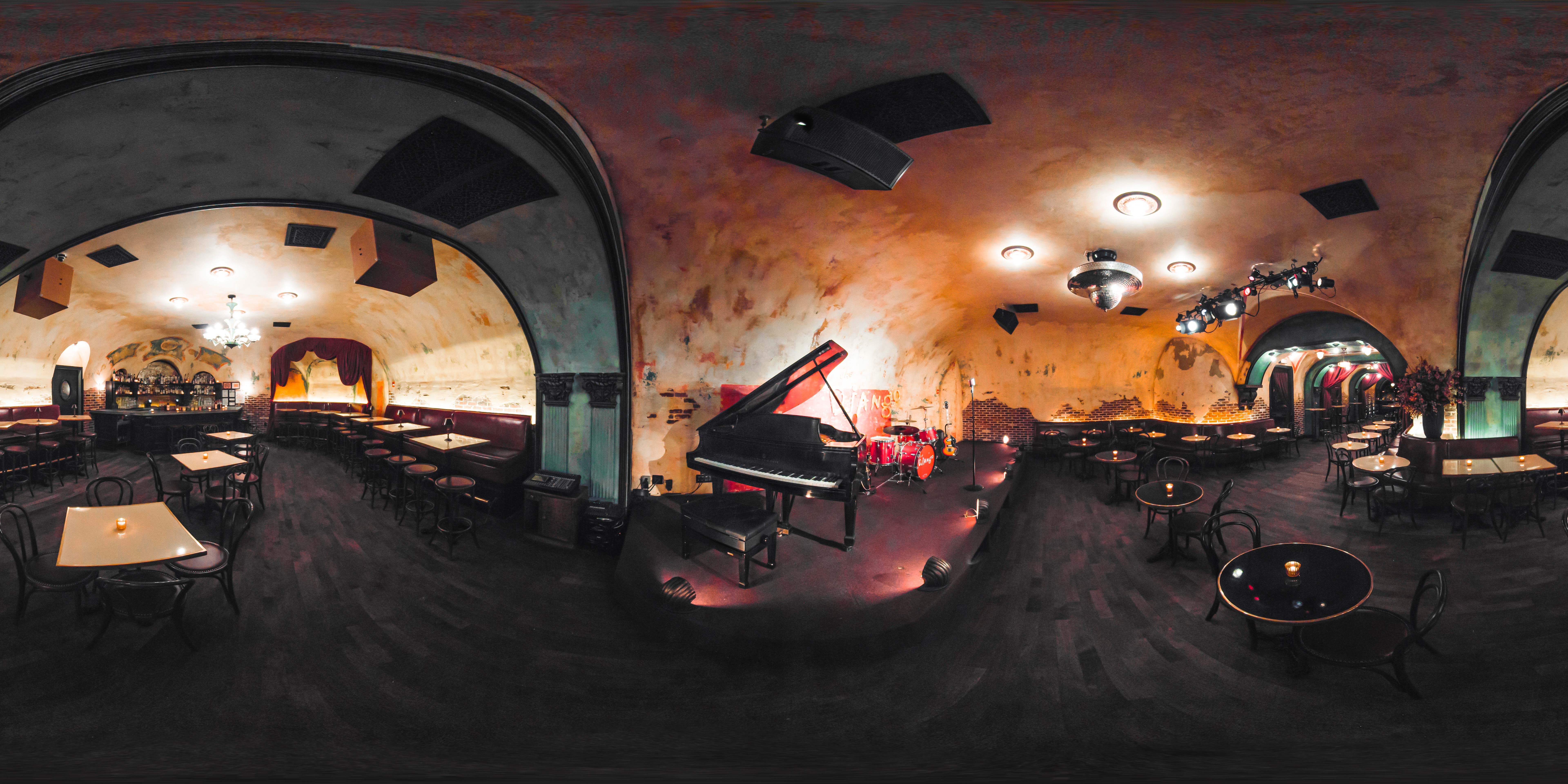 A wide-angle view of a dining area with a grand piano, arched windows, and a vaulted ceiling.