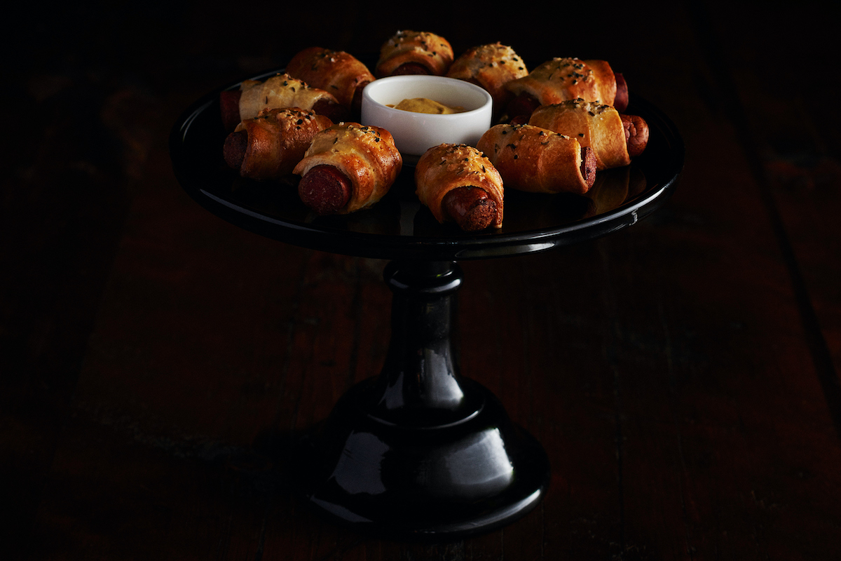 pigs in a blanket are arranged on a serving tray with mustard