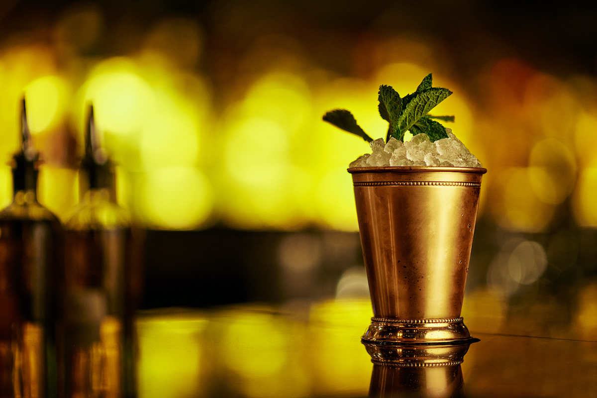 a mojito in a bronze glass garnished with mint leaves sits on top of a bar