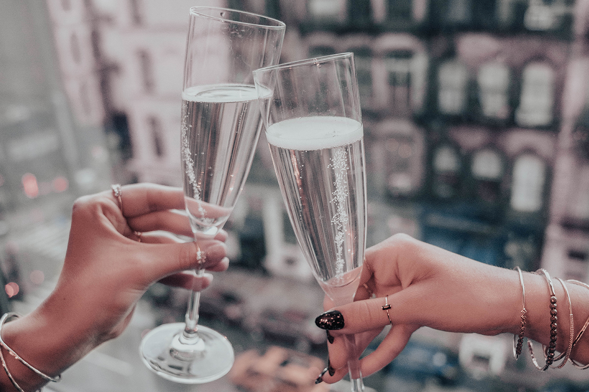 two women hold up flutes of champagne in a toast. The Tribeca neighborhood view can be seen outside the window