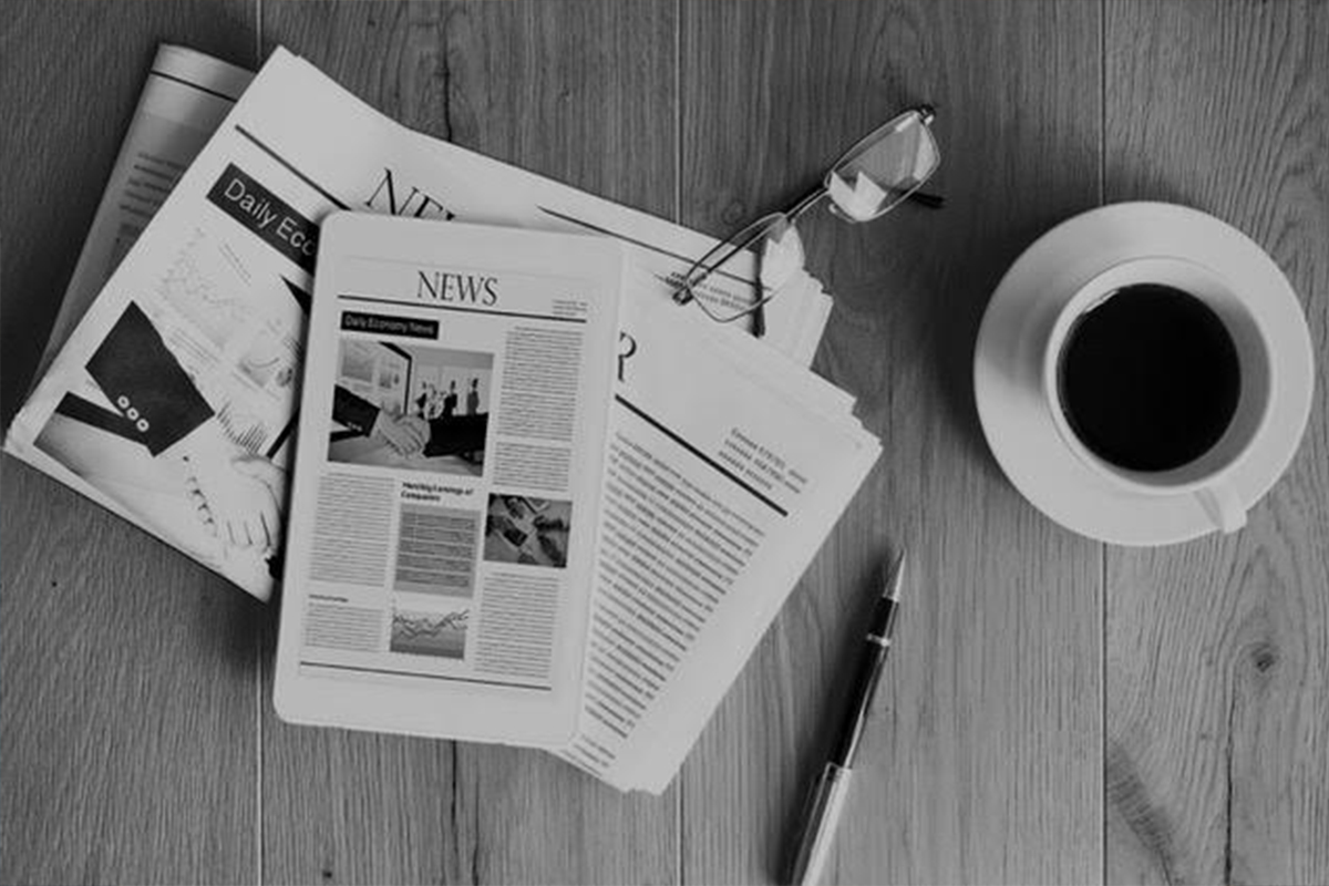 a black and white image of a coffee cup next to a pile of newspapers and pens