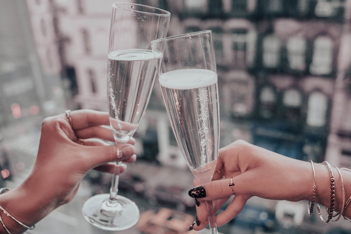 two women hold up flutes of champagne in a toast. The Tribeca neighborhood view can be seen outside the window
