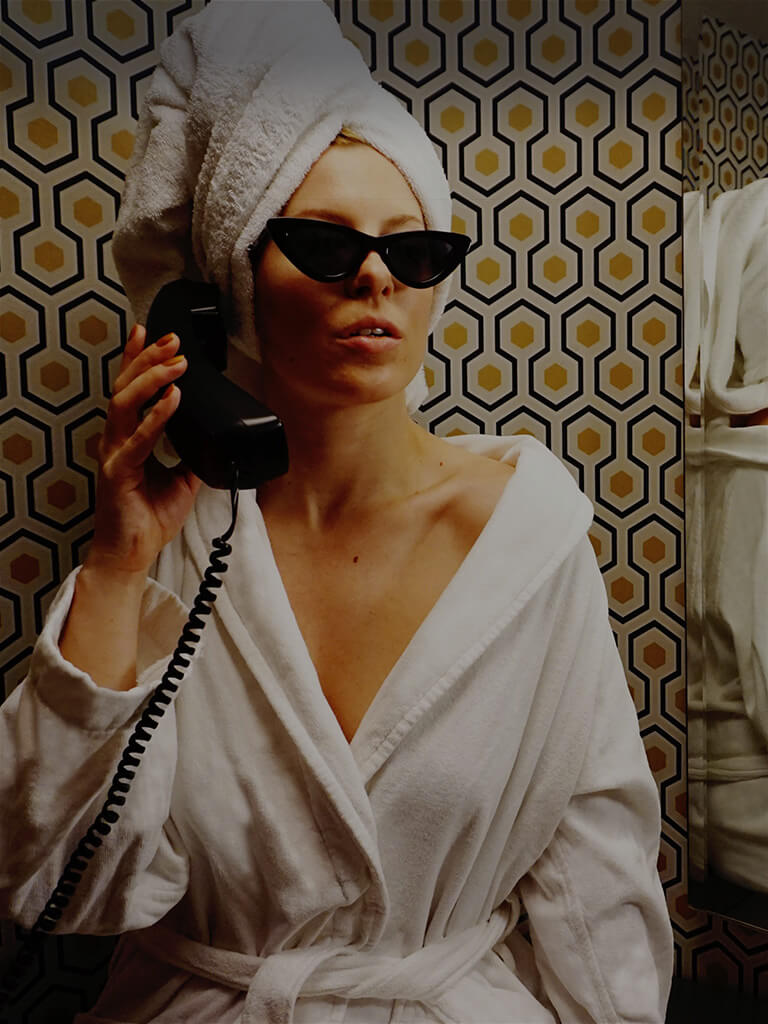 woman in a white robe and sunglasses talks on a retro phone