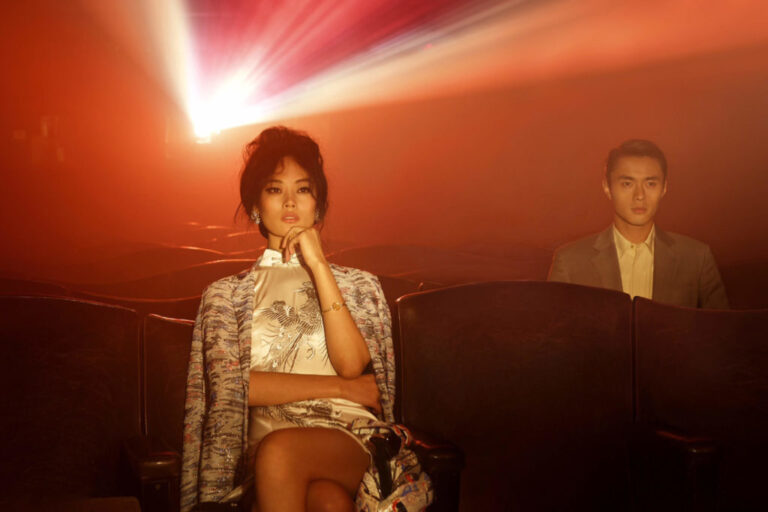 a man and a woman dressed in their best sit at a theatre watching a show