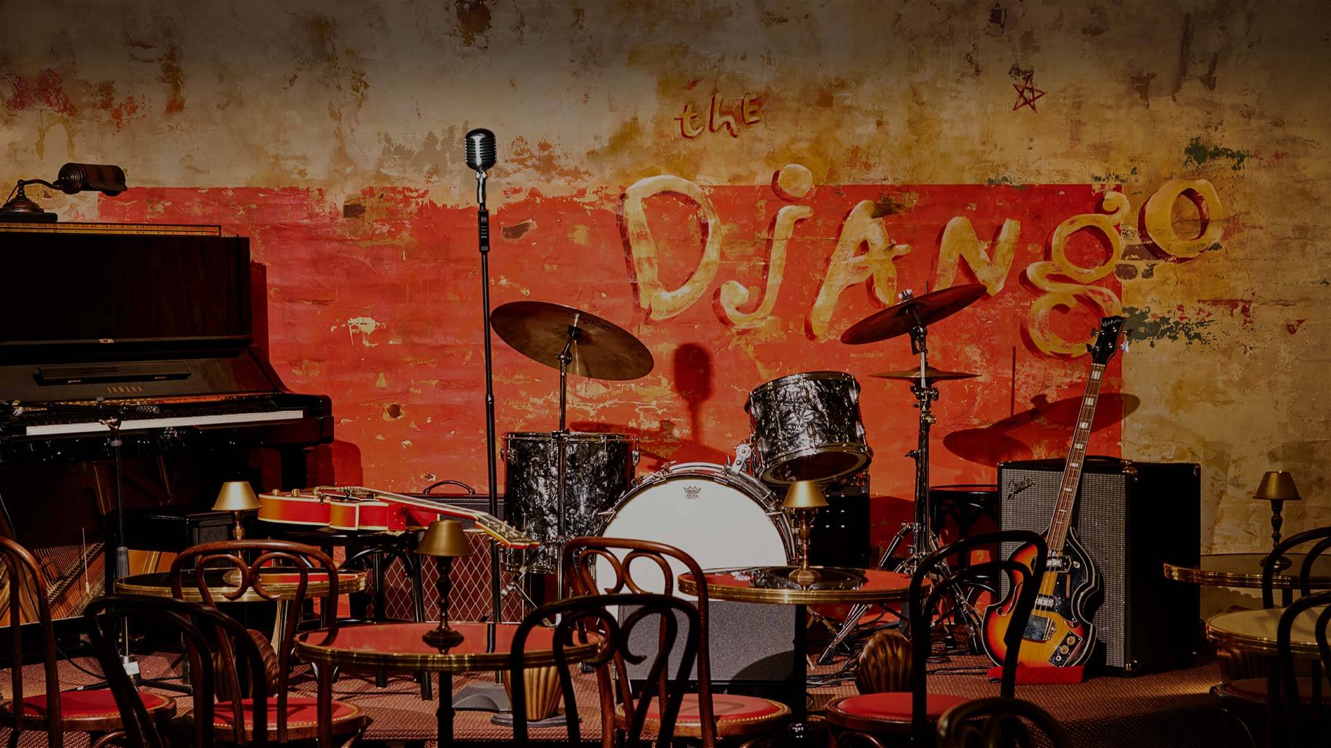A lounge with a piano, drums, guitar, and microphone for live music performances.