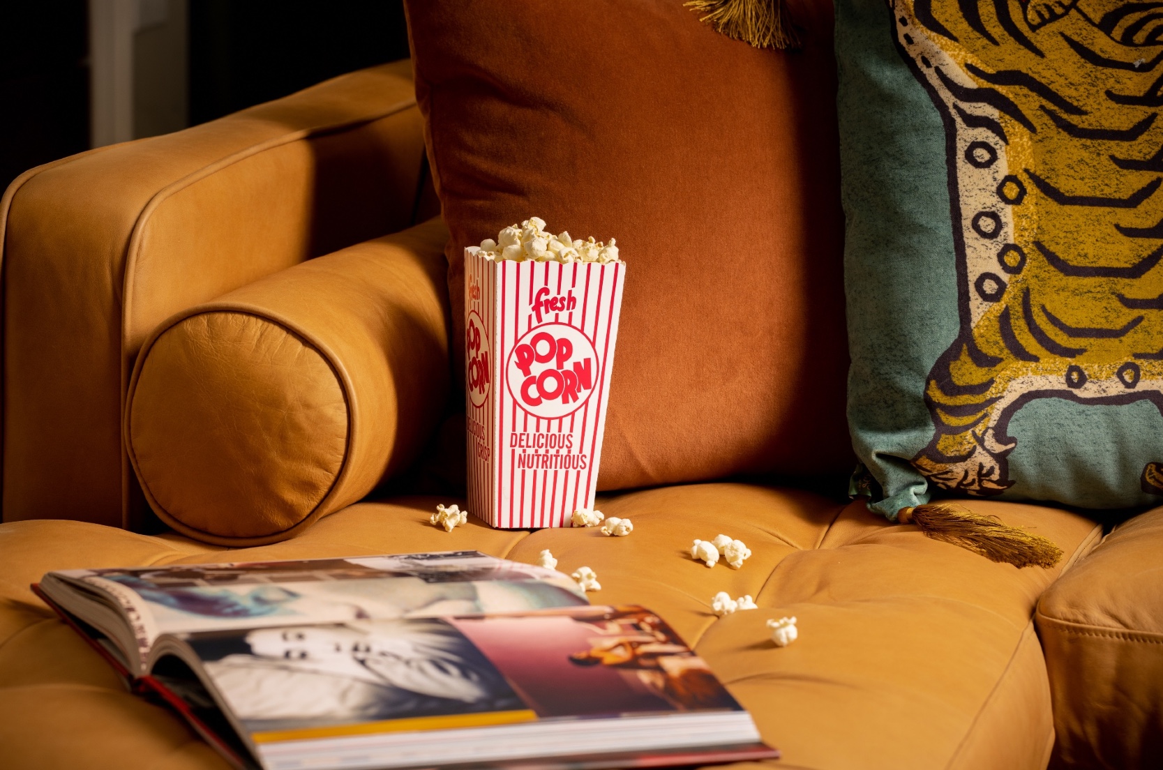 Popcorn and open book on a brown couch.