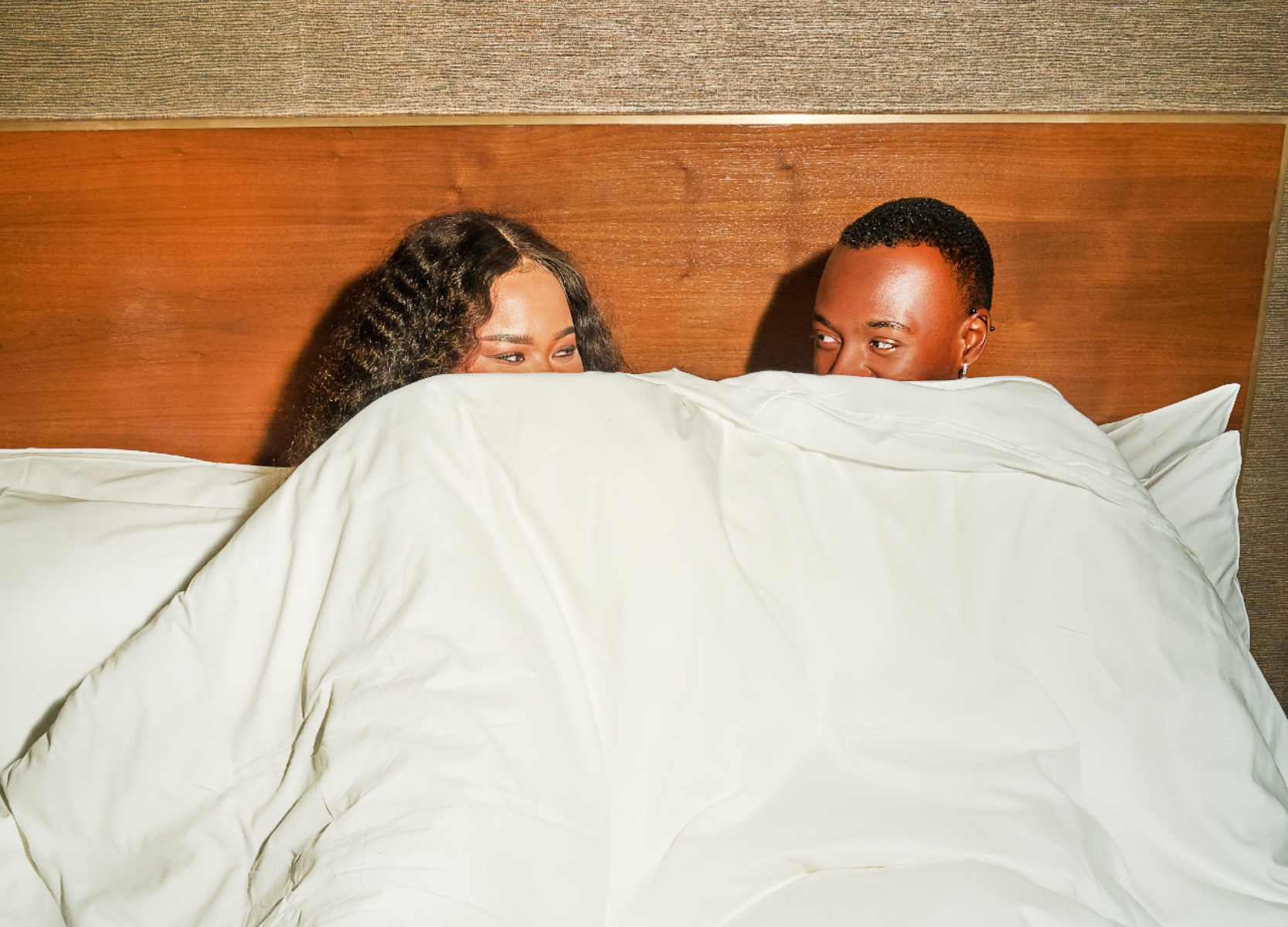 Couple in bed at Roxy Hotel holding the covers up to their faces.