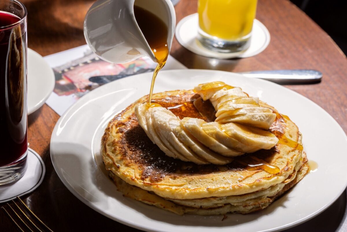 Pouring syrup over banana covered pancakes.