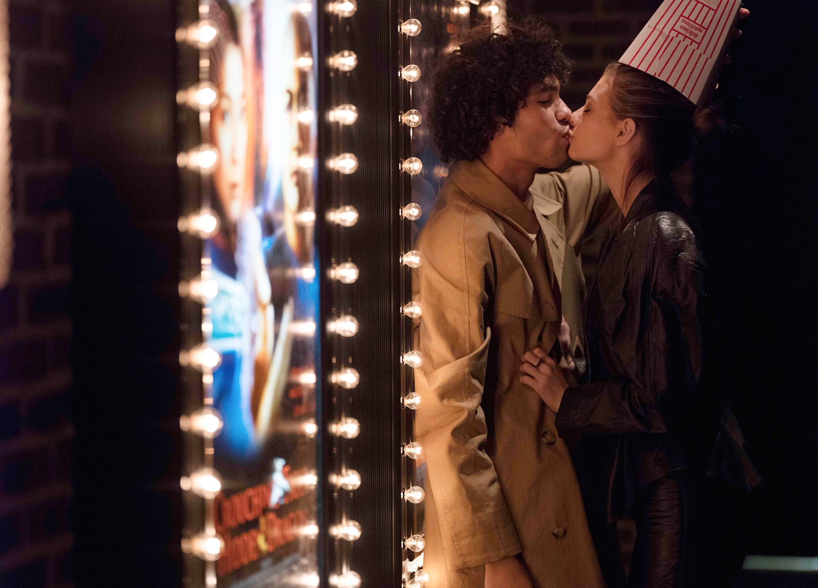 Man and woman kissing in front of a movie theater poster lightbox.