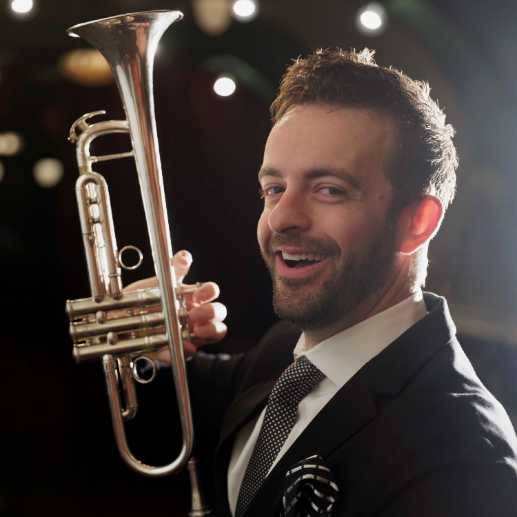 Musician Benny Benack singing at The Django at the microphone while holding a trumpet.