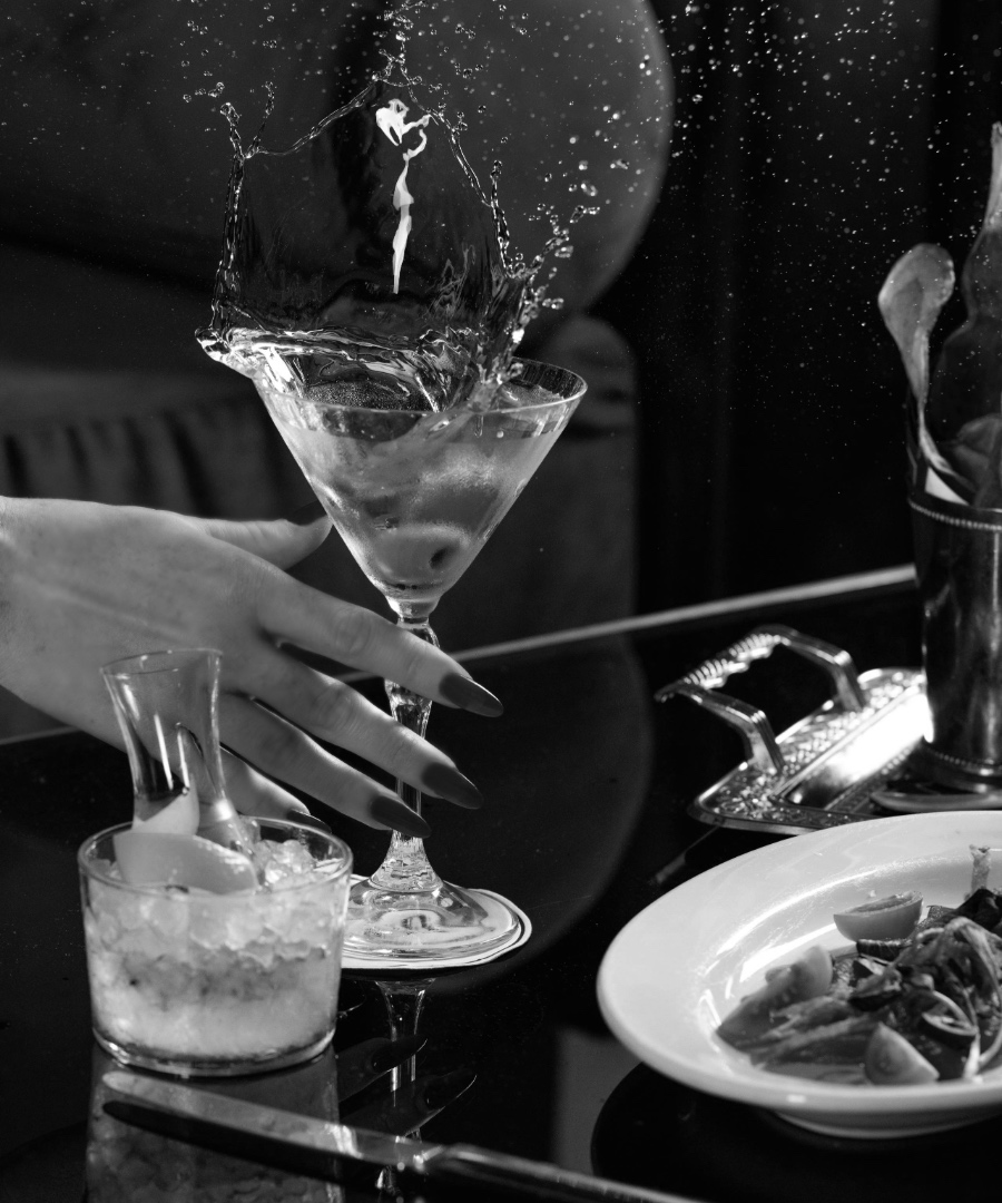 Woman's hand reaching for a martini glass with splashing liquid.