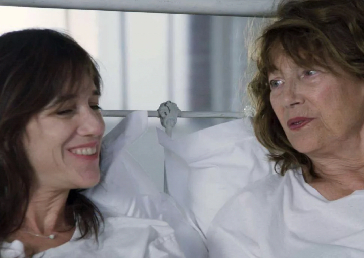 an image of two women in white sit on a bed and talk to each other