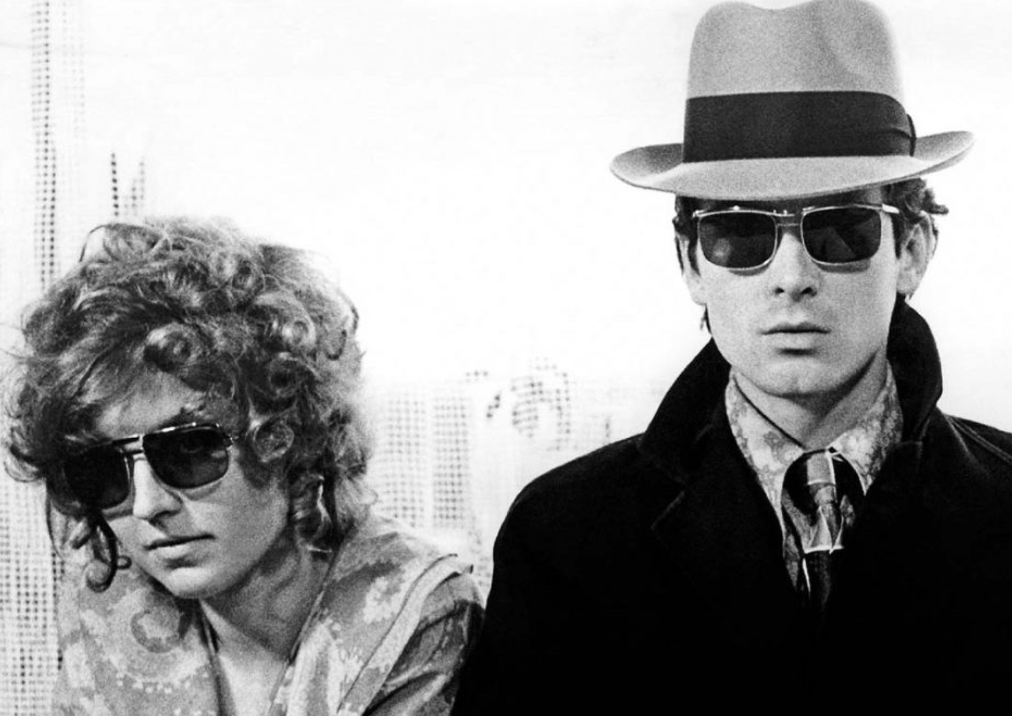a black and white photograph of a man and a woman wearing disguises walking towards the camera . the skyline of a city is in the background